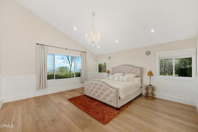 bedroom featuring a notable chandelier, a decorative wall, light wood-style flooring, wainscoting, and vaulted ceiling