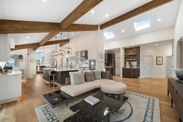 living area with high vaulted ceiling, light wood-style flooring, a skylight, beam ceiling, and an inviting chandelier