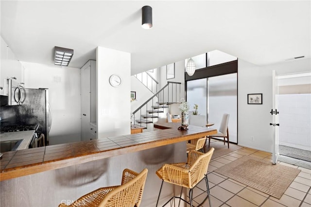 115 Bayside Pl Unit 115, Corona Del Mar, CA 92625 - kitchen featuring light tile patterned floors, visible vents, appliances with stainless steel finishes, tile counters, and a kitchen bar