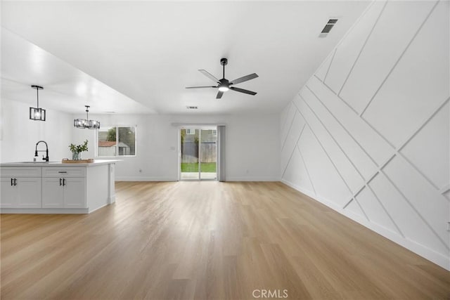 unfurnished living room featuring light wood-type flooring, visible vents, a sink, and ceiling fan with notable chandelier