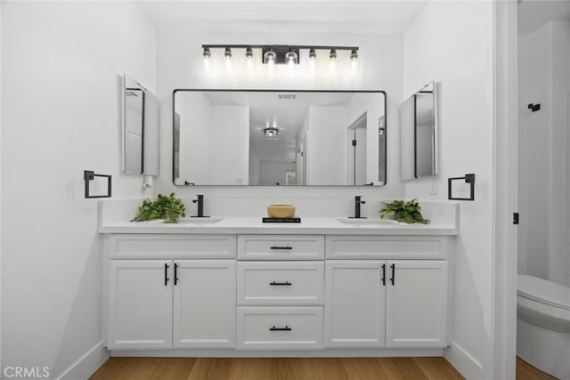 bathroom featuring toilet, double vanity, a sink, and wood finished floors