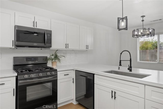 kitchen with a sink, white cabinets, light countertops, black appliances, and pendant lighting