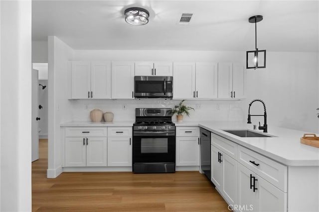 kitchen with white cabinets, hanging light fixtures, light countertops, black appliances, and a sink