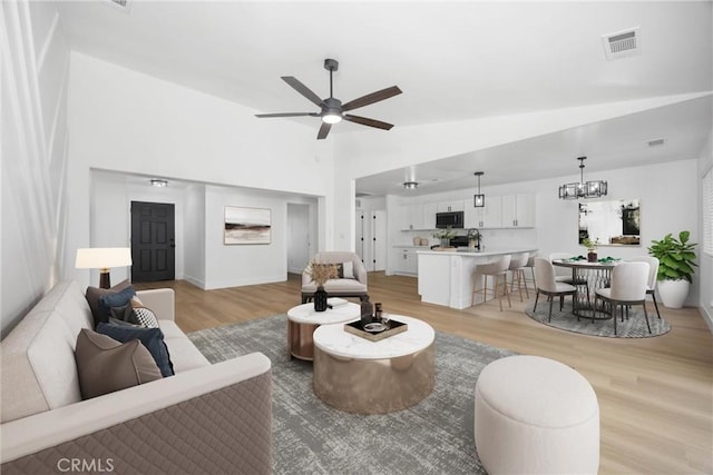 living room featuring ceiling fan with notable chandelier, high vaulted ceiling, light wood-style flooring, and visible vents