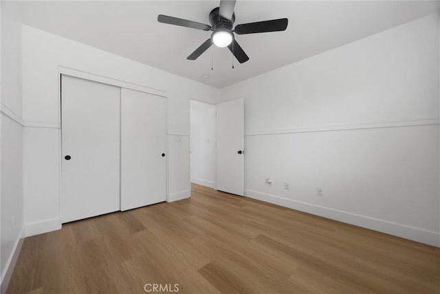 unfurnished bedroom featuring a ceiling fan, a closet, light wood-style flooring, and baseboards