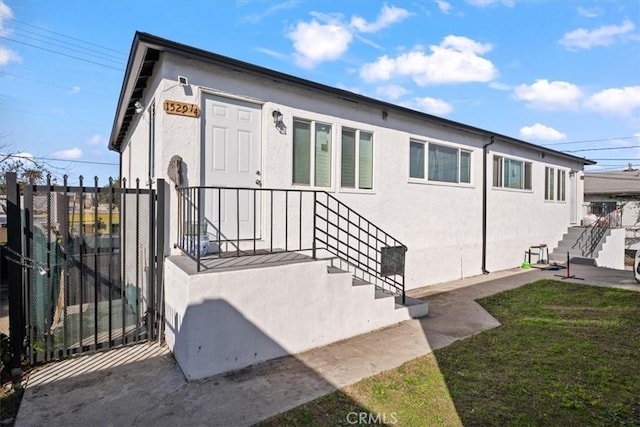 view of exterior entry with a gate, a yard, fence, and stucco siding