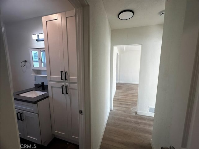 corridor featuring light wood-type flooring, visible vents, baseboards, and a sink