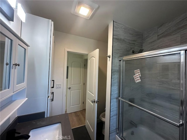 full bath featuring toilet, shower / bath combination with glass door, wood finished floors, and vanity