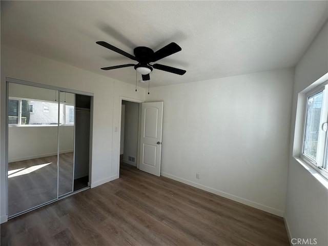 unfurnished bedroom featuring a closet, dark wood finished floors, a ceiling fan, and baseboards