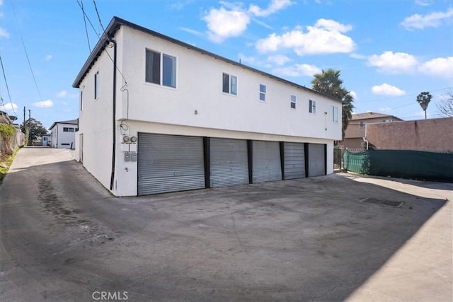 rear view of house with a garage, fence, and stucco siding