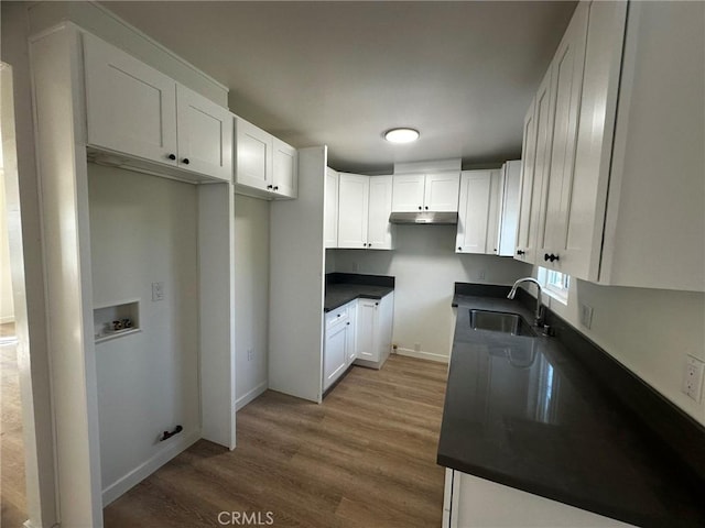 kitchen with dark countertops, wood finished floors, under cabinet range hood, white cabinetry, and a sink