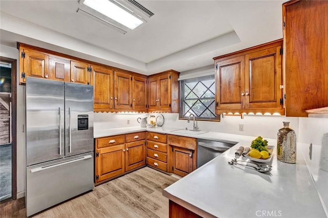 kitchen featuring stainless steel appliances, a sink, light countertops, light wood-type flooring, and brown cabinets