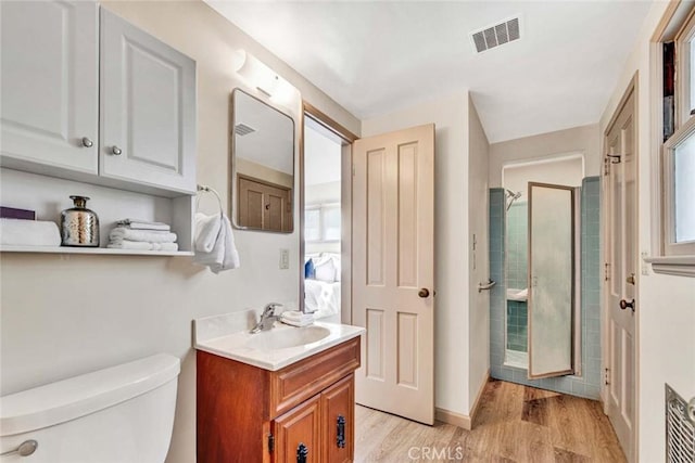 bathroom with a stall shower, visible vents, toilet, wood finished floors, and vanity