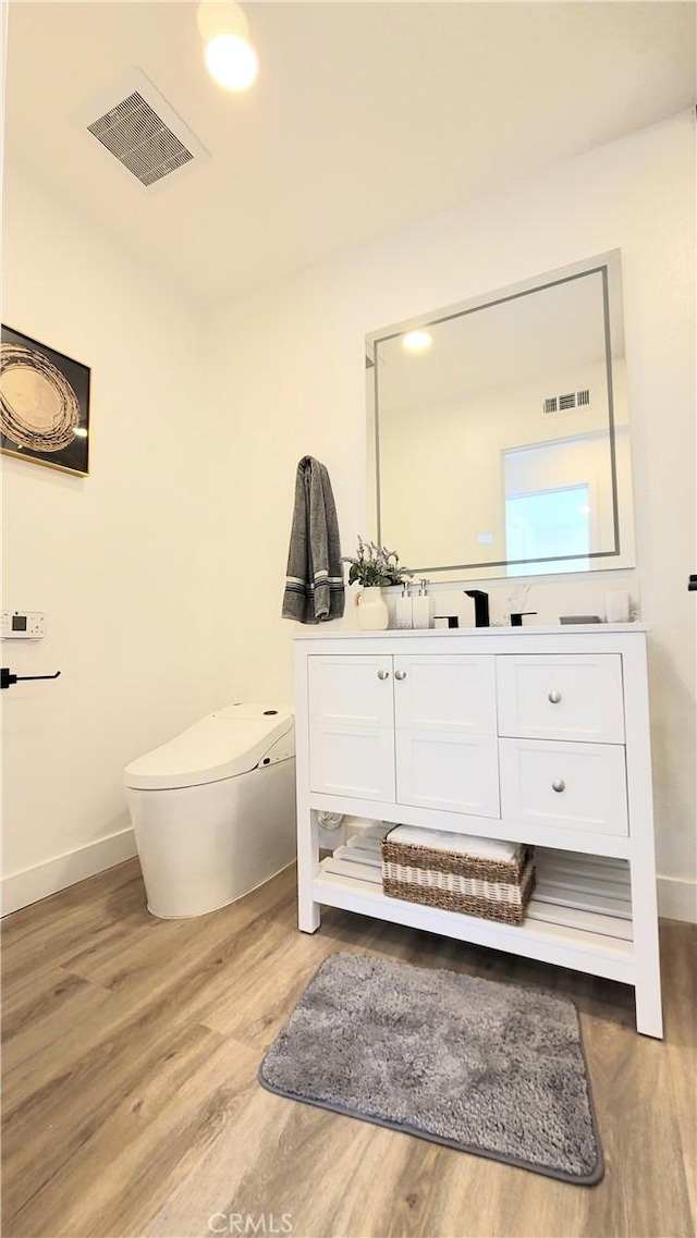 bathroom featuring visible vents, vanity, baseboards, and wood finished floors