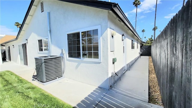 view of side of property with a patio, a fenced backyard, central air condition unit, a yard, and stucco siding