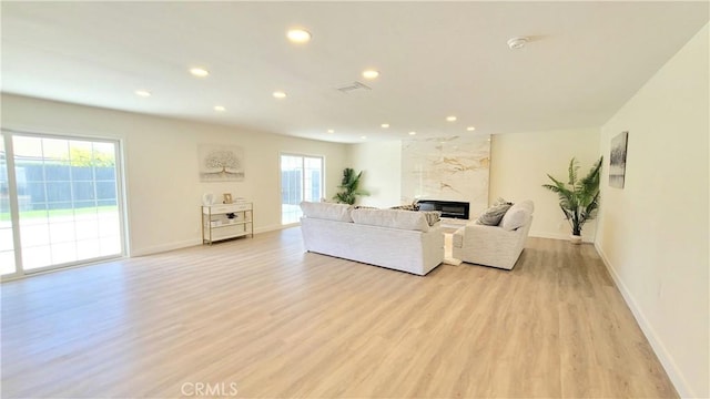 living area with light wood-style floors, a premium fireplace, visible vents, and recessed lighting