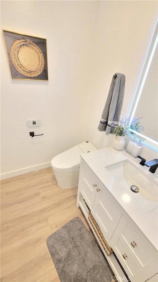 bathroom with toilet, wood finished floors, vanity, and baseboards