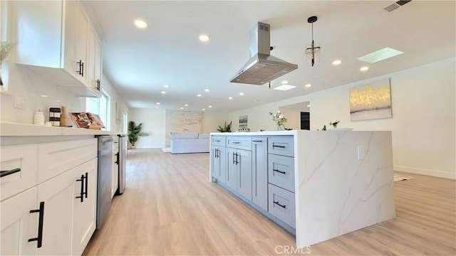 kitchen featuring light wood-style flooring, white cabinetry, open floor plan, and decorative light fixtures