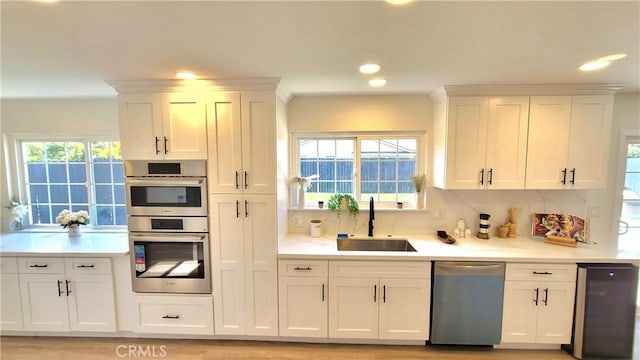 kitchen featuring stainless steel appliances, light countertops, a sink, and white cabinetry