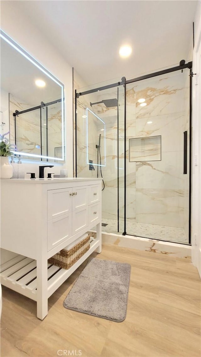 full bath with a marble finish shower, wood finished floors, and vanity