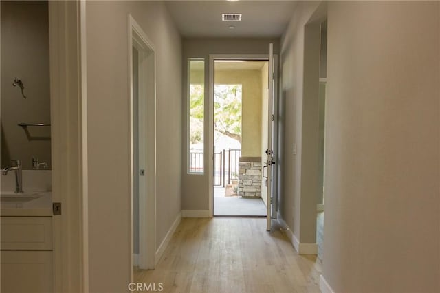 doorway to outside with light wood-style floors, visible vents, a sink, and baseboards