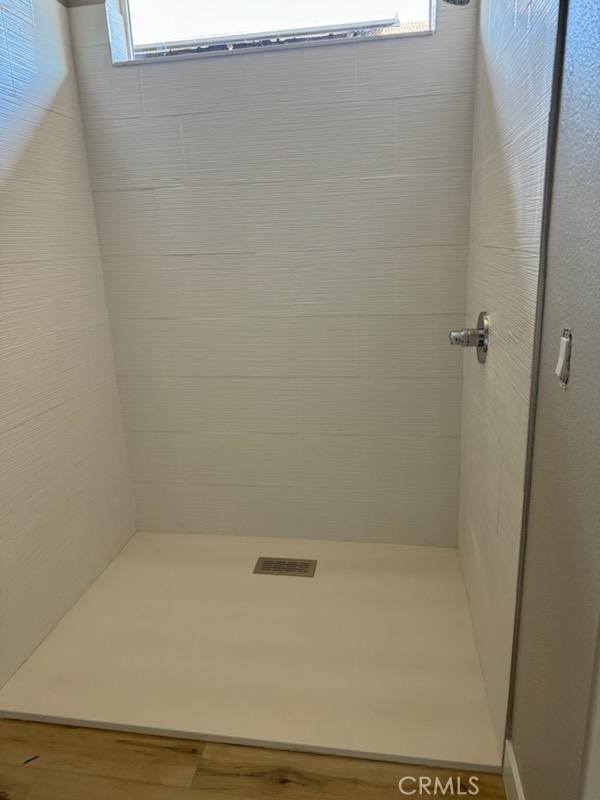 bathroom with tiled shower, plenty of natural light, and wood finished floors