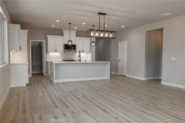 kitchen featuring a center island with sink, stainless steel microwave, light countertops, and decorative light fixtures