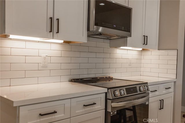 kitchen with white cabinetry, light stone counters, stainless steel appliances, and backsplash