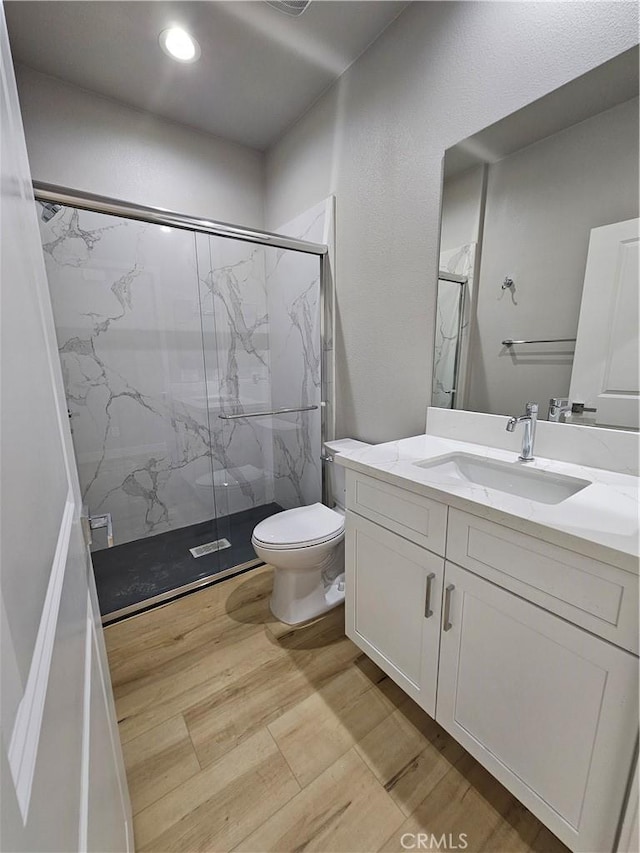 bathroom with a marble finish shower, recessed lighting, toilet, vanity, and wood finished floors