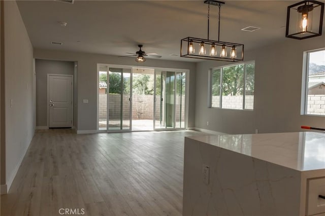 interior space with visible vents, a ceiling fan, light wood-style flooring, and baseboards