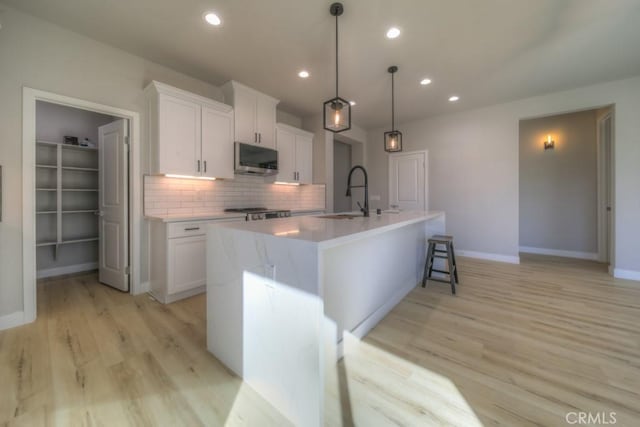 67813 Rio Vista Dr, Cathedral City, CA 92234 - kitchen with stainless steel microwave, white cabinets, backsplash, light wood-type flooring, and a center island with sink