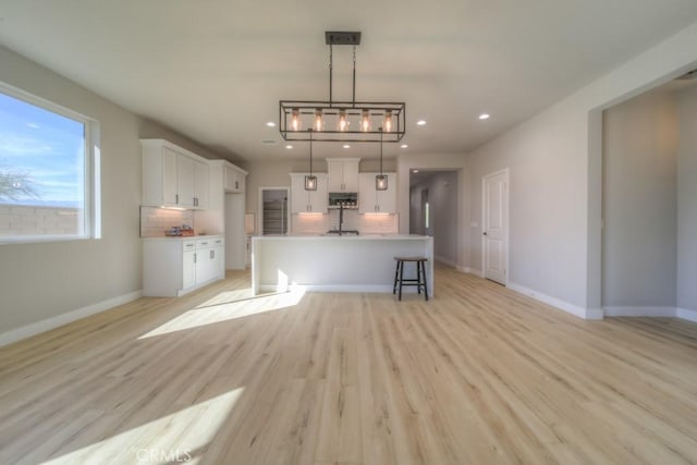 67813 Rio Vista Dr, Cathedral City, CA 92234 - kitchen featuring backsplash, stainless steel microwave, light wood-type flooring, white cabinets, and pendant lighting