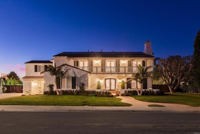 mediterranean / spanish-style house featuring a balcony, fence, french doors, a chimney, and a front yard