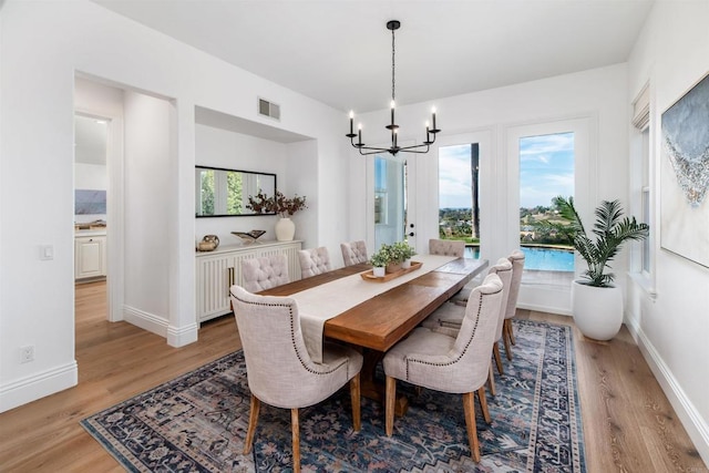 dining area featuring baseboards, visible vents, a notable chandelier, and light wood finished floors