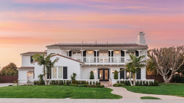 mediterranean / spanish home with a front lawn, french doors, a balcony, and roof mounted solar panels