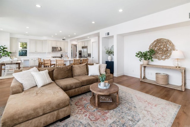 living room featuring visible vents, baseboards, wood finished floors, and recessed lighting