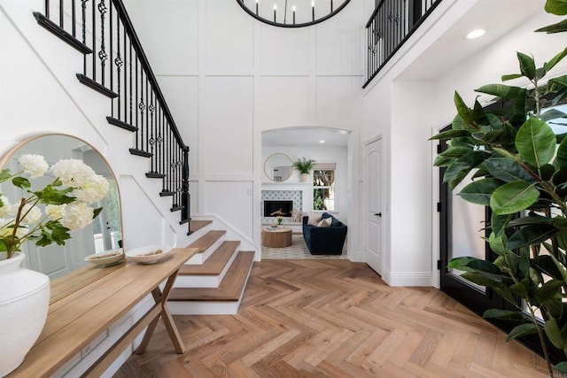 foyer entrance featuring arched walkways, a towering ceiling, stairway, a fireplace, and a decorative wall