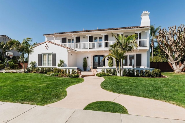 mediterranean / spanish-style house with a balcony, french doors, stucco siding, a chimney, and a front yard