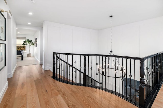 corridor featuring recessed lighting, light wood-style flooring, a chandelier, and an upstairs landing