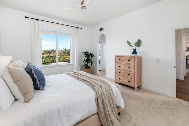 bedroom with baseboards, visible vents, arched walkways, light colored carpet, and ceiling fan