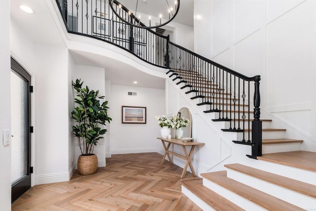 foyer entrance featuring visible vents, a chandelier, a towering ceiling, and baseboards