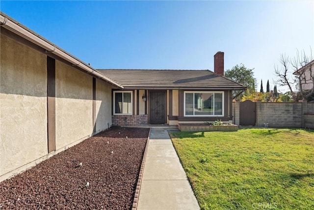 entrance to property featuring a yard, fence, a chimney, and stucco siding