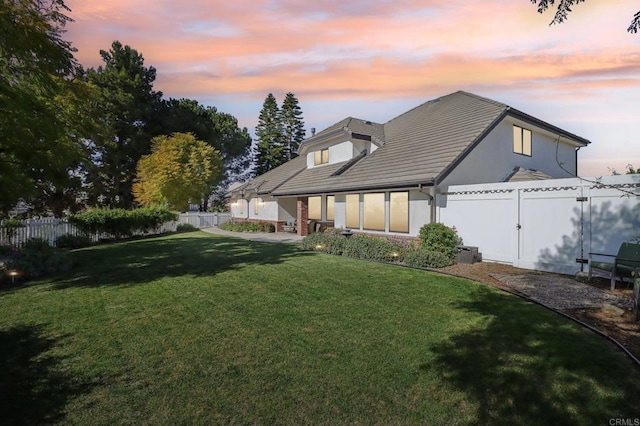 back of property at dusk with a yard, a patio area, a fenced backyard, and stucco siding