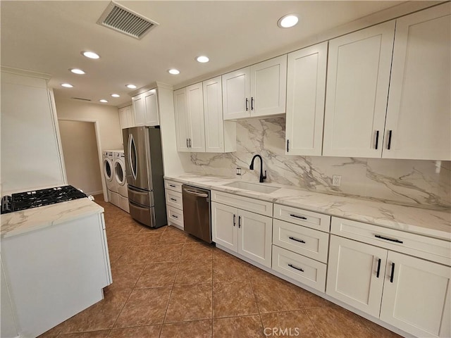 kitchen featuring stainless steel appliances, visible vents, white cabinetry, a sink, and independent washer and dryer