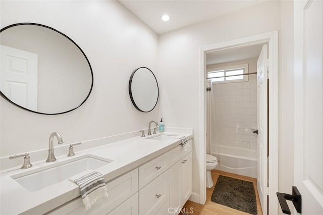 bathroom featuring toilet, double vanity, a sink, and wood finished floors