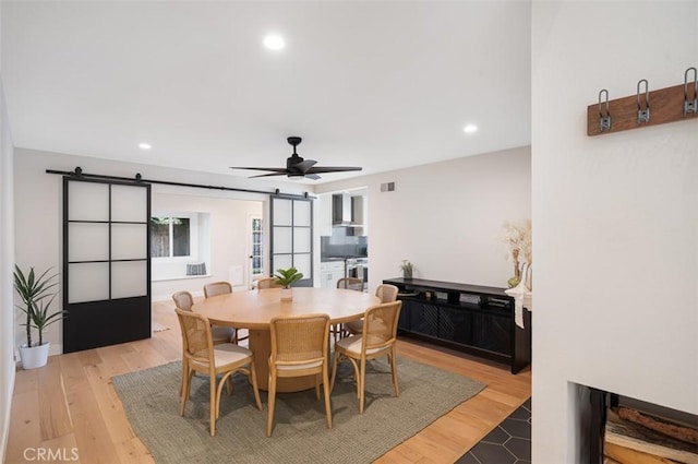 dining area with a ceiling fan, light wood-type flooring, recessed lighting, and a barn door