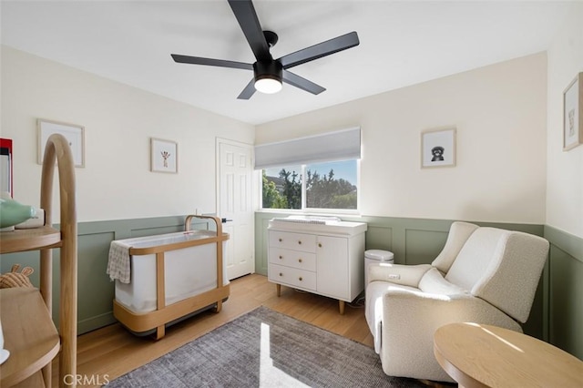 bedroom featuring wainscoting, wood finished floors, a ceiling fan, and a decorative wall