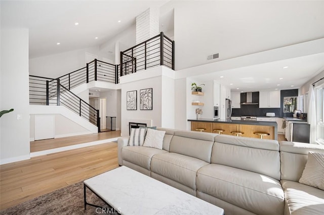 living room featuring light wood finished floors, visible vents, a towering ceiling, stairway, and recessed lighting