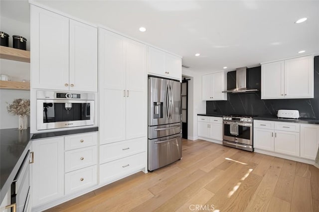 kitchen featuring stainless steel appliances, open shelves, light wood-type flooring, wall chimney exhaust hood, and dark countertops