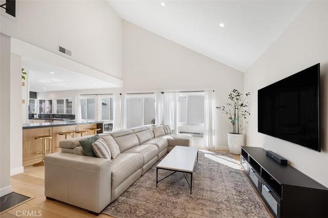 living area with high vaulted ceiling, light wood-style flooring, recessed lighting, visible vents, and baseboards